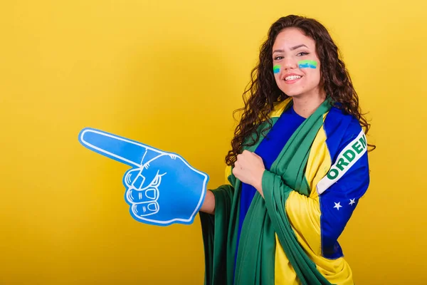 Woman soccer fan, fan of brazil, world cup, wearing foam glove. pointing to negative space, ad, text or advertising. Left side.