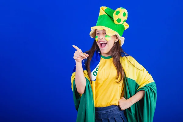 ブラジルのサッカーファンの少女です 帽子と旗に身を包んだ 遠くに何かを向け — ストック写真