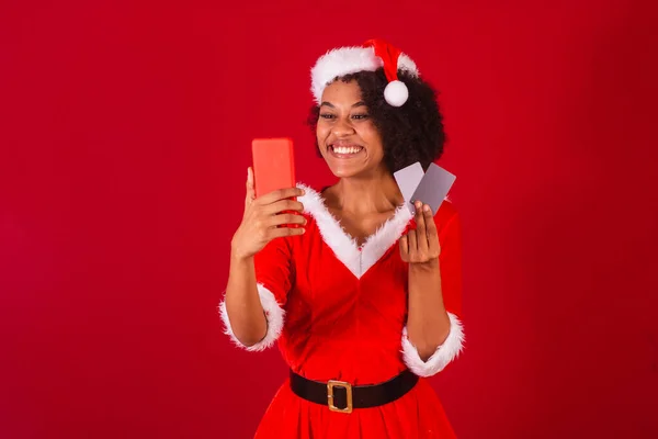 漂亮的巴西黑人女人 穿着圣塔克洛斯 妈妈克洛斯的衣服 拿着智能手机和信用卡 — 图库照片