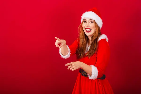美しいブラジルの赤髪の女性 クリスマス服を着て サンタクロース 遠くの何かを指差して — ストック写真