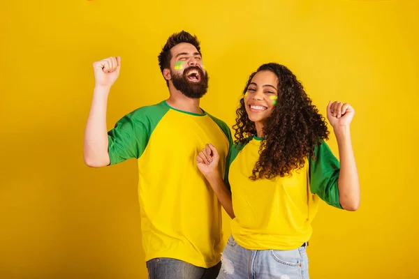 stock image couple of brazil soccer supporters, dressed in the colors of the nation, black woman, caucasian man. Twisting and vibrating.