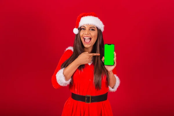 漂亮的巴西女人穿着圣诞服装 圣诞老人 手持显示绿色彩色屏幕的智能手机 — 图库照片