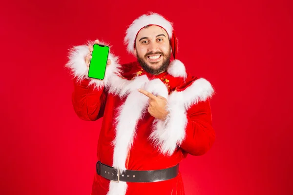サンタクロースの服を着たブラジル人男性が緑色のクロマスクリーンでスマートフォンを持ち — ストック写真