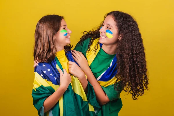 sisters and friends who support Brazil, football fans, smiling and looking at each other watching the Brazil game. World Cup. Olympics.
