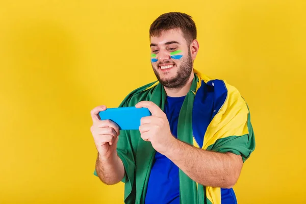 Fã de futebol brasileiro adulto usando smartphone de bandeira assistindo  jogo pelo celular streaming online