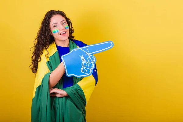 Woman soccer fan, fan of brazil, world cup, wearing foam glove. pointing to negative space, ad, text or advertising. Right side.