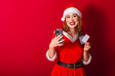 Güzel Brezilyalı kızıl saçlı kadın, Noel kıyafetleri giymiş, Noel Baba. Elinde kredi kartları ve akıllı telefon vardı..