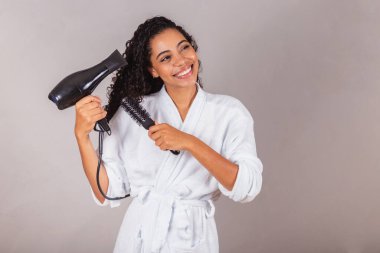 Güzel Brezilyalı siyah kadın, bornoz ve havlu giyiyor. Saç kurutma makinesi, fırça, spa, güzellik merkezi, saç bakımı..