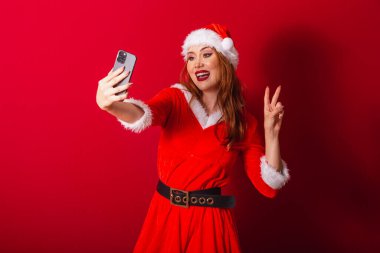 Güzel Brezilyalı kızıl saçlı kadın, Noel kıyafetleri giymiş, Noel Baba. akıllı telefondan video çağrısı.