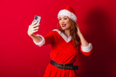 Güzel Brezilyalı kızıl saçlı kadın, Noel kıyafetleri giymiş, Noel Baba. akıllı telefondan video çağrısı.
