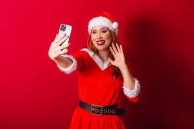Güzel Brezilyalı kızıl saçlı kadın, Noel kıyafetleri giymiş, Noel Baba. akıllı telefondan video çağrısı.