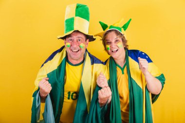 Yetişkin bir çift, Brezilyalı futbol taraftarı, bayrak ve şapka takıyorlar. Birlikte gol atıyoruz..