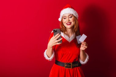Güzel Brezilyalı kızıl saçlı kadın, Noel kıyafetleri giymiş, Noel Baba. Elinde kredi kartları ve akıllı telefon vardı..