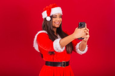 Noel kıyafetleri giymiş güzel Brezilyalı kadın, Noel Baba. Akıllı telefon kutlaması..