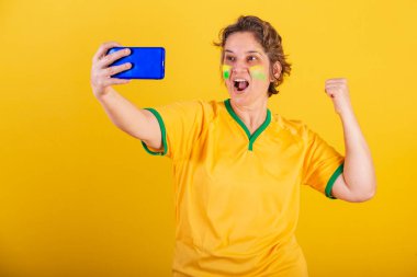 Yetişkin bir kadın, Brezilya futbolu fanatiği, akıllı telefon, cep telefonuyla futbol maçı izleyen,.