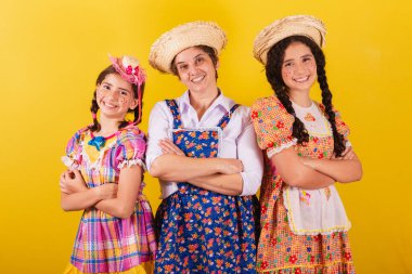 Büyükannesi ve iki torunu tipik Festa Junina kıyafetleri giymişler. Kollar çapraz, gülümseyen, mutlu.