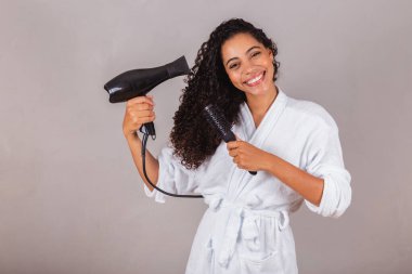 Güzel Brezilyalı siyah kadın, bornoz ve havlu giyiyor. Saç kurutma makinesi, fırça, spa, güzellik merkezi, saç bakımı..