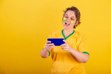 Yetişkin bir kadın, Brezilya futbol fanatiği, akıllı telefon, oyun oynuyor..