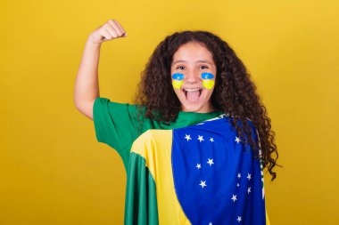 Brezilyalı, beyaz, futbol taraftarı, gülümseyen, kollarını kaldırmış, süslenmiş, güç gösteren bir kız..