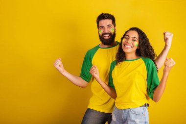 İki Brezilyalı futbol taraftarı, ulusun renginde giyinmiş, siyah kadın, beyaz erkek. Bükülüyor ve titriyor..