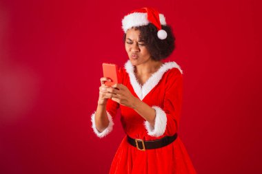 Güzel siyah Brezilyalı kadın, Noel Baba gibi giyinmiş, Mama Claus, akıllı telefondan bir şey izliyor.