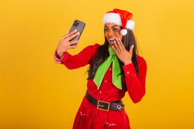 Güzel siyah Brezilyalı kadın, Noel Baba kıyafetleri içinde, akıllı telefon kendi portresini çekiyor, selfie çekiyor..