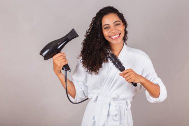 Güzel Brezilyalı siyah kadın, bornoz ve havlu giyiyor. Saç kurutma makinesi, fırça, spa, güzellik merkezi, saç bakımı..