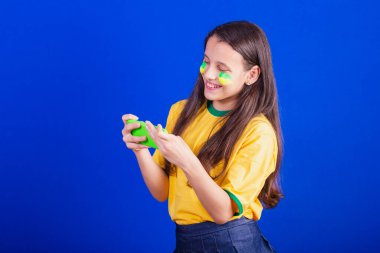 Genç bir kız, Brezilyalı bir futbol taraftarı. Cep telefonu tutmak, maç izlemek, Smartphone için tezahürat yapmak. uygulamalar.