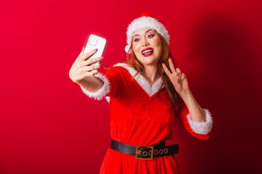 Güzel Brezilyalı kızıl saçlı kadın, Noel kıyafetleri giymiş, Noel Baba. akıllı telefondan kendi portresini çekmek.