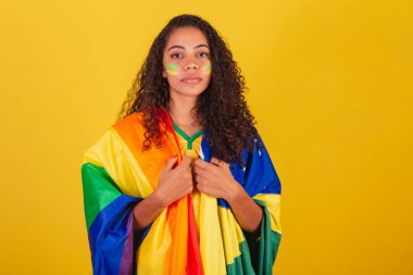 Genç siyah Brezilyalı kadın, futbol fanatiği. LGBT ve Brezilya bayrağıyla önyargılara karşı savaş. Ciddiyet