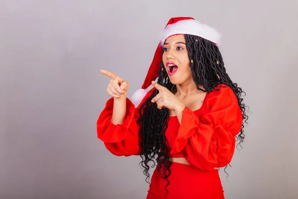 ブラジルの黒人女性はクリスマス服を着て陽気なクリスマスを笑顔で何かを指差して — ストック写真
