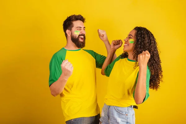 stock image couple of brazil soccer supporters, dressed in the colors of the nation, black woman, caucasian man. Twisting and vibrating.