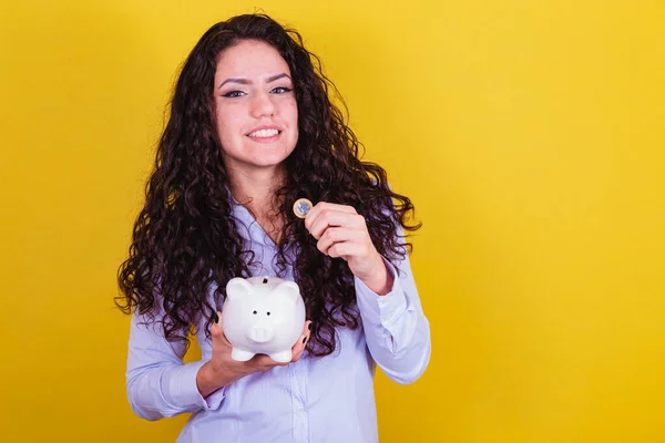 Caucasian, brazilian woman holding coin and piggy bank, concept of finance, economy, saving.