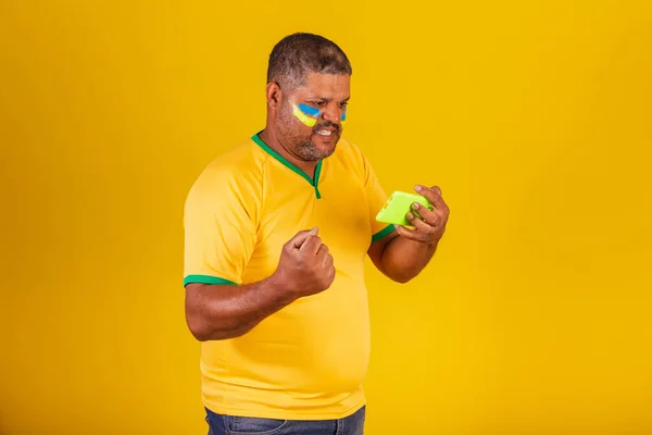 stock image Brazilian black man, soccer fan from Brazil. watching game on mobile. smartphone