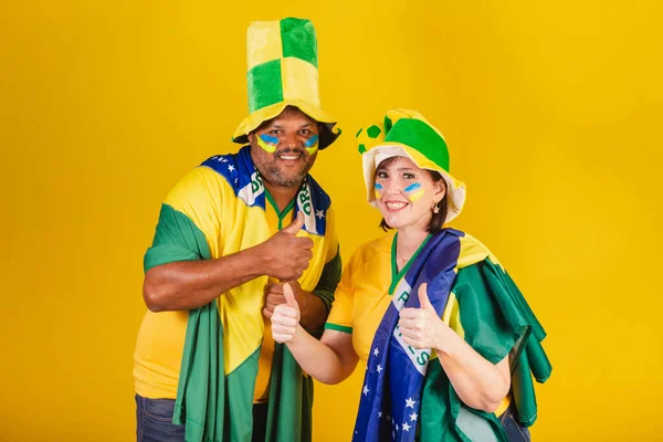 Couple, red-haired woman and black man, Brazilian soccer fans. like, thumb up, positive.