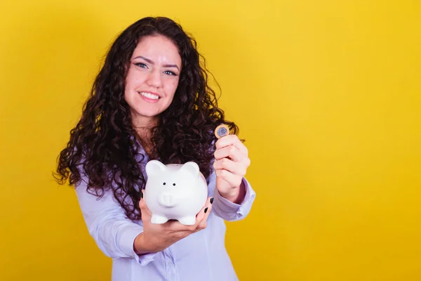 Caucasian, brazilian woman holding coin and piggy bank, concept of finance, economy, saving.