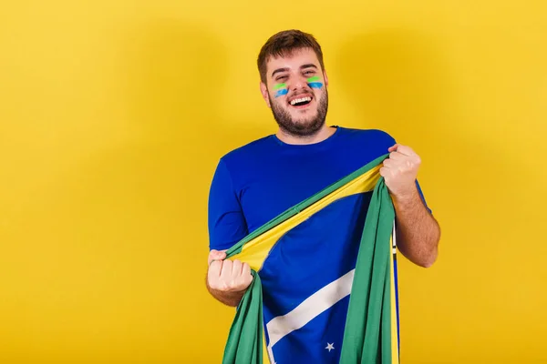 ブラジル出身のサッカーファンであるブラジル人の白人男性が喜びで応援しブラジル国旗を掲揚 — ストック写真