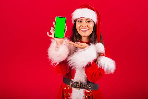 穿圣诞服装的巴西女人圣诞老人手持带有绿色屏幕的彩色智能手机 — 图库照片