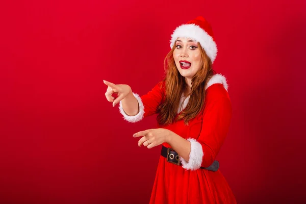 美しいブラジルの赤髪の女性 クリスマス服を着て サンタクロース 遠くの何かを指差して — ストック写真