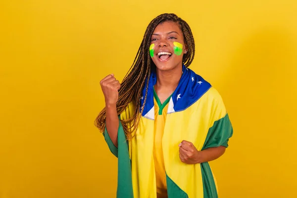 stock image black woman young brazilian soccer fan. wearing flag, celebrating victory, shouting yes.