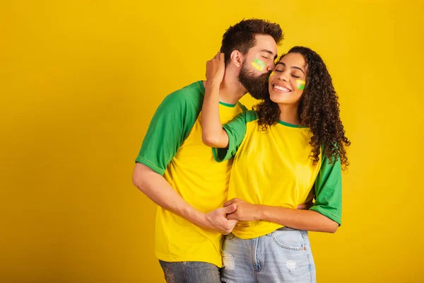couple of brazil soccer supporters, dressed in the colors of the nation, black woman, caucasian man. kissing, love.