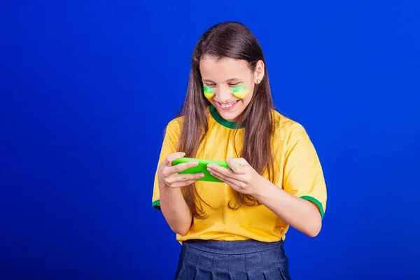 ブラジルのサッカーファンの少女です 携帯電話を持ったりゲームを見たりスマートフォンを応援したり アプリケーション — ストック写真