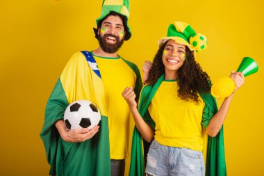 İki Brezilyalı futbol taraftarı, ulusun renginde giyinmiş, siyah kadın, beyaz erkek. bayrak ve aksesuarlar kullanarak