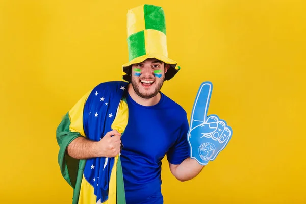 ブラジル人の白人男性ブラジル人サッカーファン帽子と泡の指を身に着けて応援し笑顔 — ストック写真