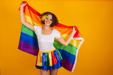 Güzel Brezilyalı kadın, karnaval kıyafetleri, renkli etek ve beyaz gömlek giymiş. Rimel takıyor, lgbt bayrağı taşıyor..