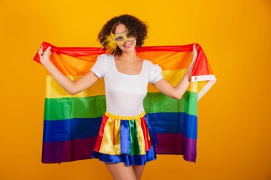 Güzel Brezilyalı kadın, karnaval kıyafetleri, renkli etek ve beyaz gömlek giymiş. Rimel takıyor, lgbt bayrağı taşıyor..