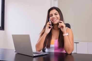 Ofiste çalışan güzel beyaz Brezilyalı iş kadını, defter. Cep telefonundan konuşuyor.