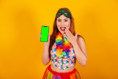 Brezilya 'lı kızıl saçlı, karnaval elbiseli, boynunda çiçeklerden bir kolyeyle, yeşil renkli ekranlı bir akıllı telefonu gösteriyor..