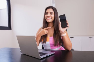 Ofiste çalışan güzel beyaz Brezilyalı iş kadını, cep telefonunu gösteriyor..