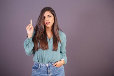 Yatay fotoğraf. Güzel Brezilyalı kadın, günlük kıyafetler, kot pantolon ve yeşil gömlekli. Fikir işareti, cevap ver.